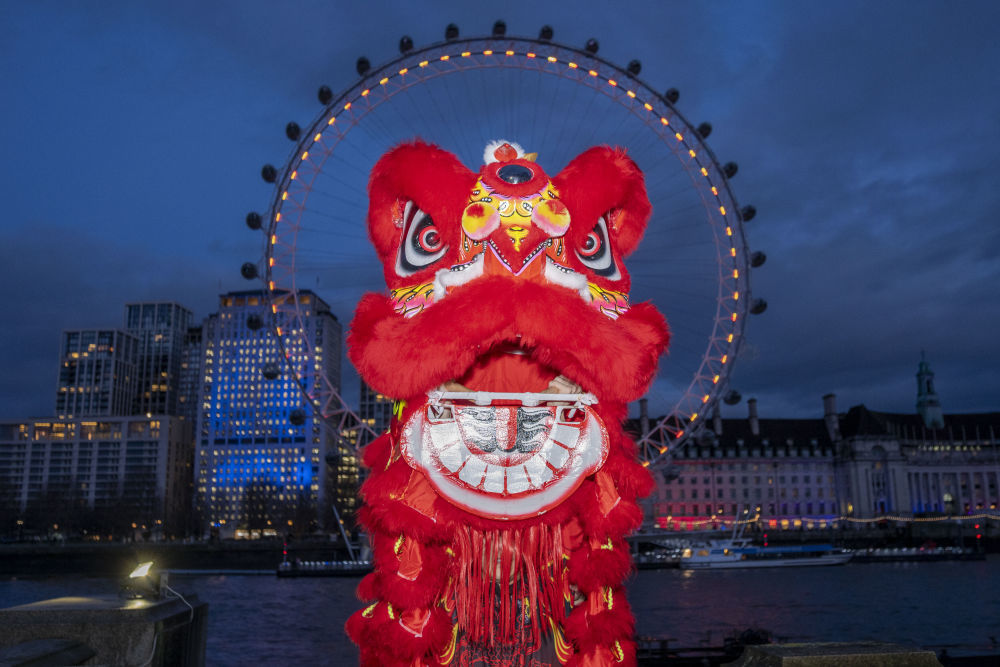 2月16日晚，在英国首都伦敦，演员在亮起红色灯光的“伦敦眼”前表演舞狮。新华社发（史蒂芬·程摄）