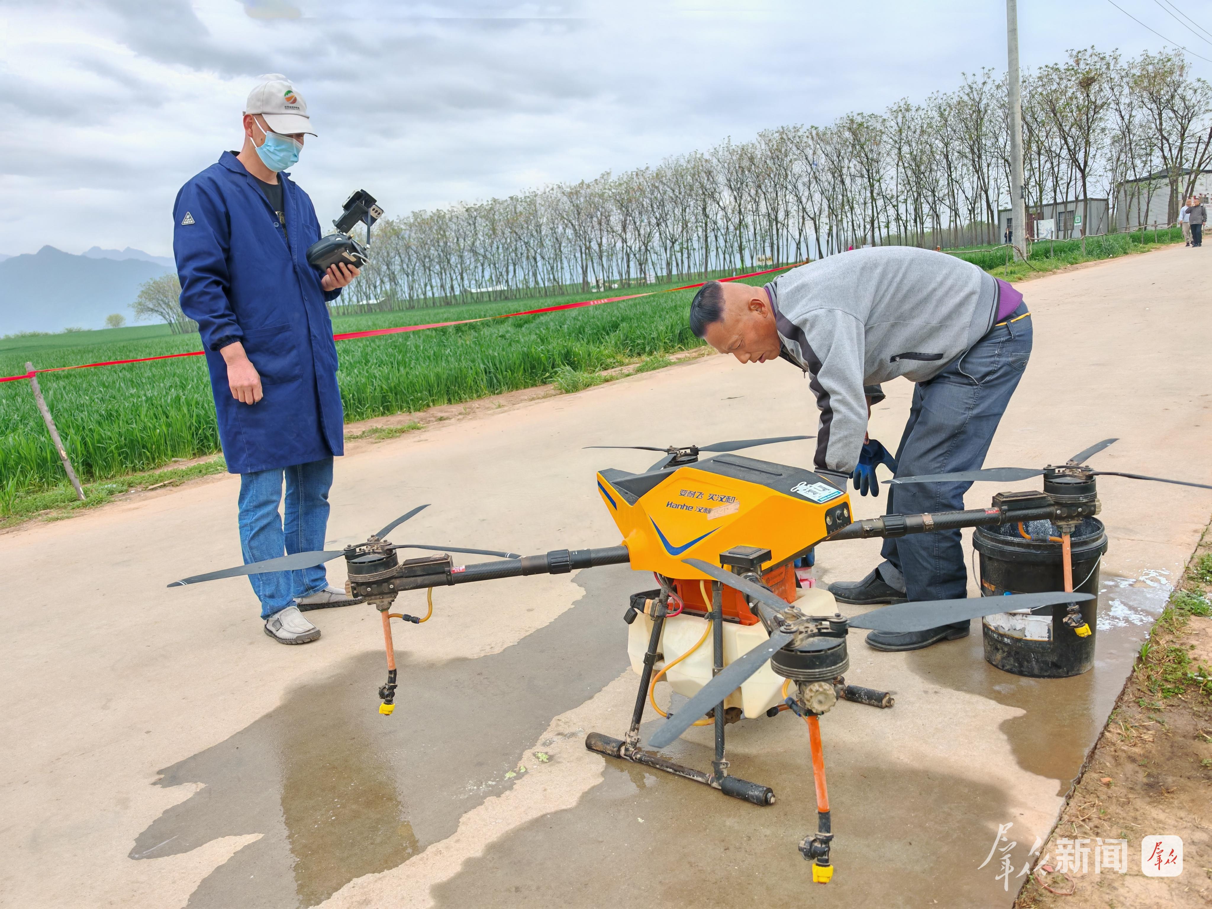 4月11日,在西安市长安区王曲街道中江兆村,长丰农机专业合作社员工(右)正在给无人机加药。群众新闻记者 王海涛摄
